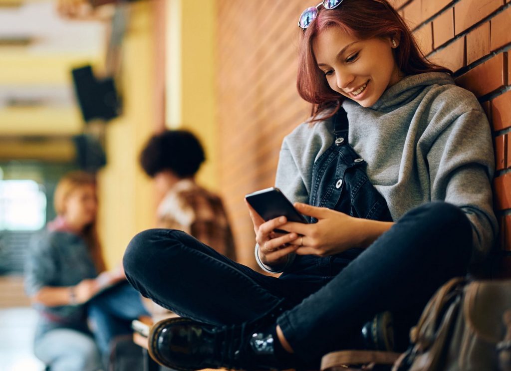 Banking-App - Fröhliches Teenager-Mädchen benutzt Smartphone
